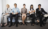 Pessoas sentadas em fileiras, como para uma entrevista de emprego, demonstrando ser um pessoal qualificado para o cargo em questão.