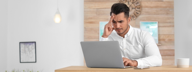 Imagem de um homem sentado a frente de um computador, aparentemente em uma sala comercial. Ele está com expressão de preocupação olhando para a tela do notebook pelos problemas para abrir sua empresa.