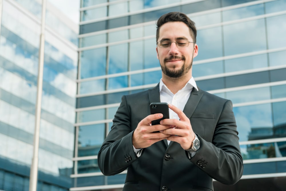 Homem sorrindo enquanto mexe no celular em frente ao trabalho, venha para a Solução
